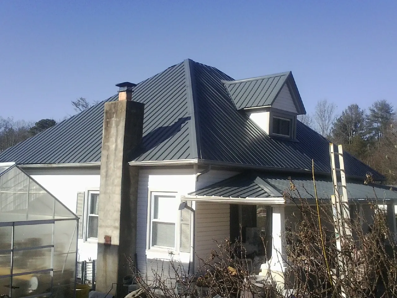 Dark blue standing seam metal roof on a white farmhouse with dormer — Slate & Tile Roof Repair by Roofing Brothers in Montville