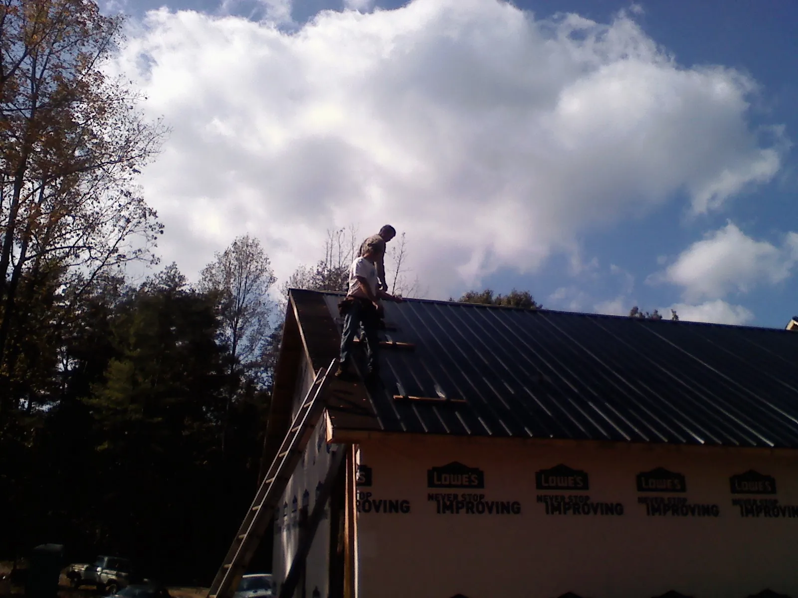 Roofer fastening dark metal panels high against a cloudy sky, from a Roof Inspection job in Montville
