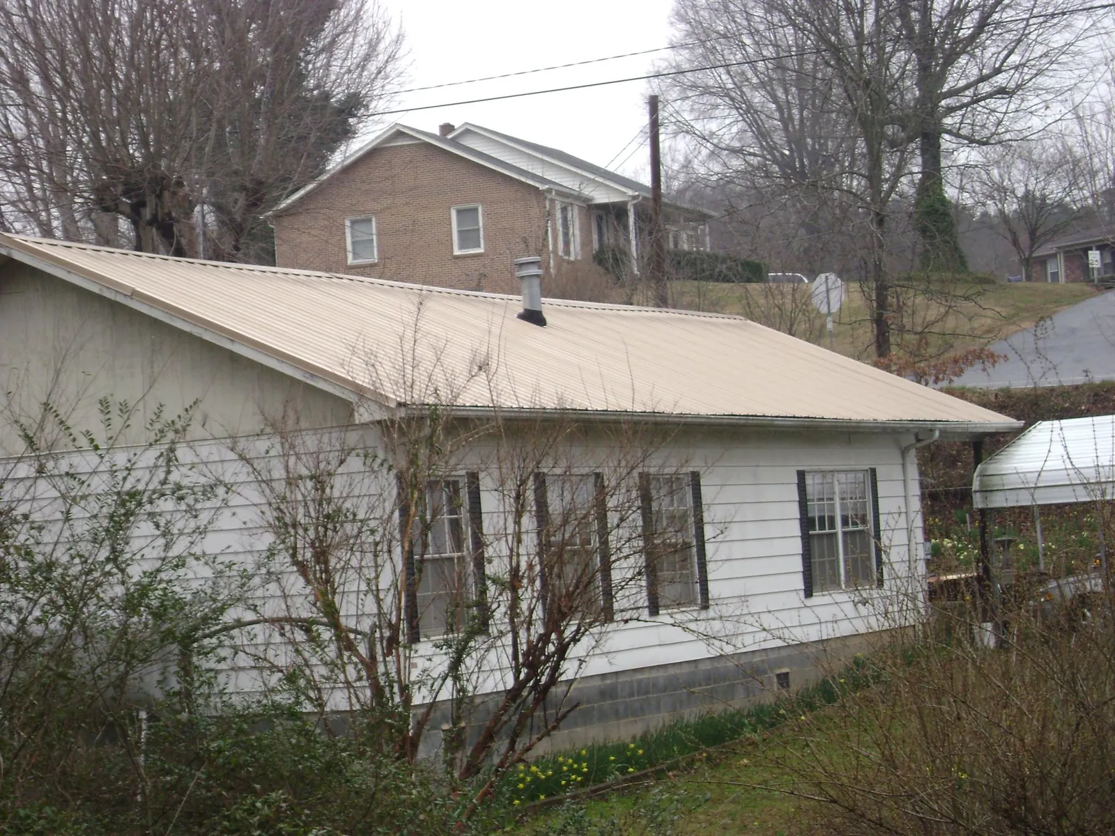 Tan metal roof on a white sided house set into a hillside — Commercial Roofing by Roofing Brothers in Montville